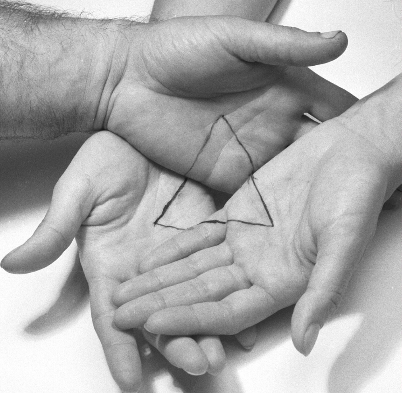 Black and white photo showing three hands interlocked, with a triangle drawn across the three.