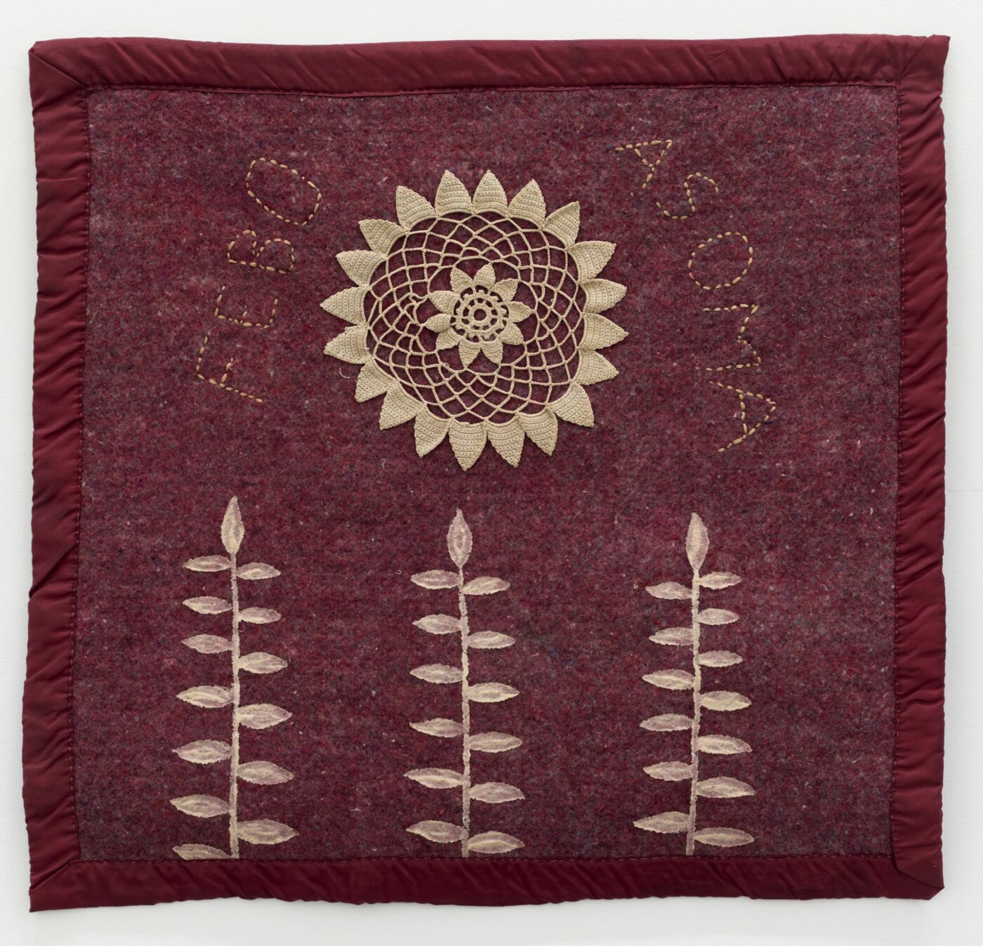 Dark red blanket with white stitched depictions of a sun and three vertical tree branches.