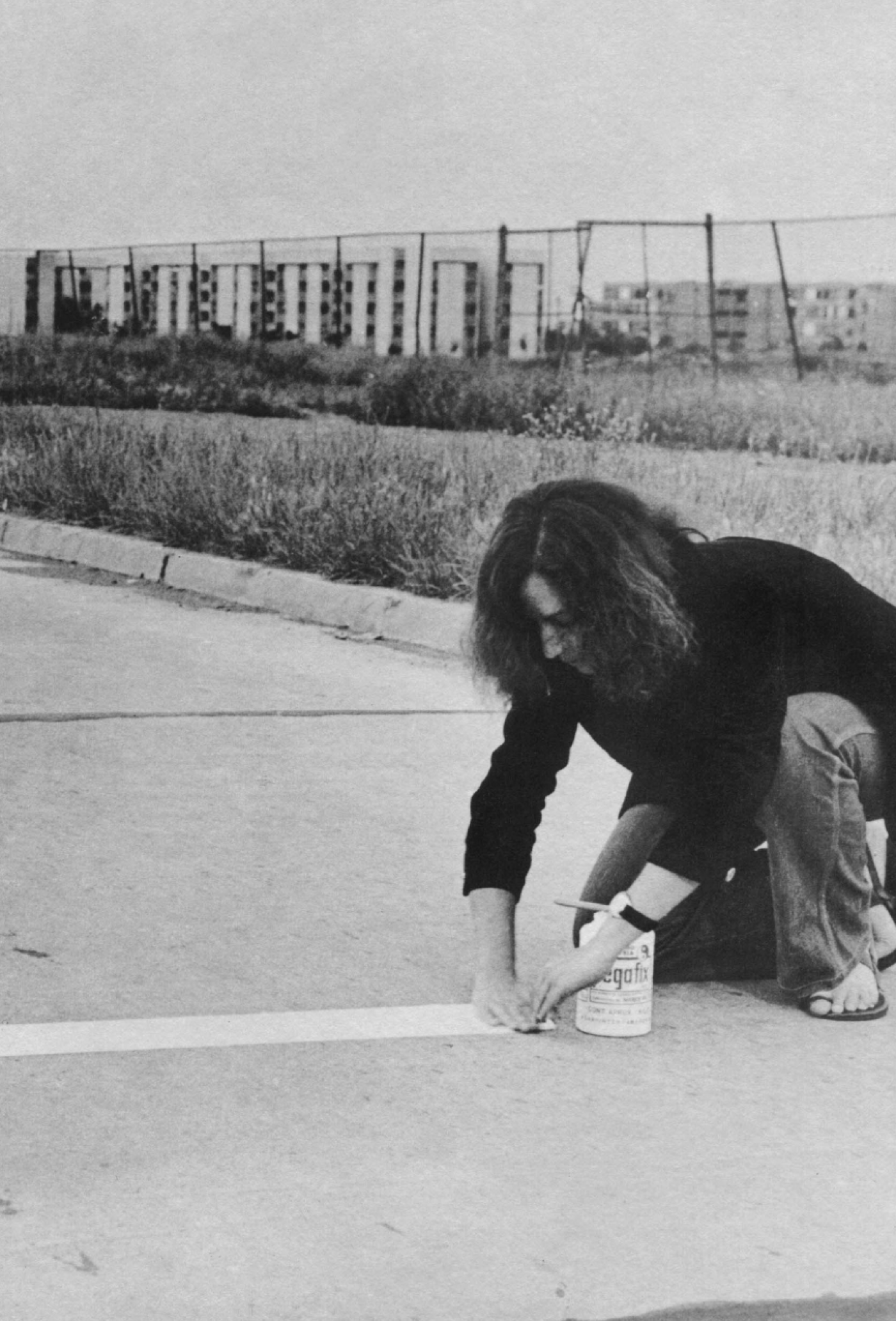 Black and white photograph of a woman painting a white line on a sidewalk.
